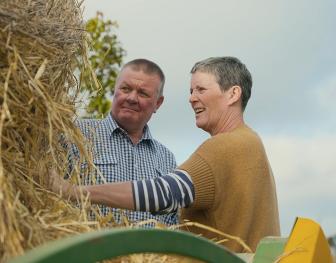 Mark and Julie Peucker standing together and smiling as they inspect a hay bale on their property