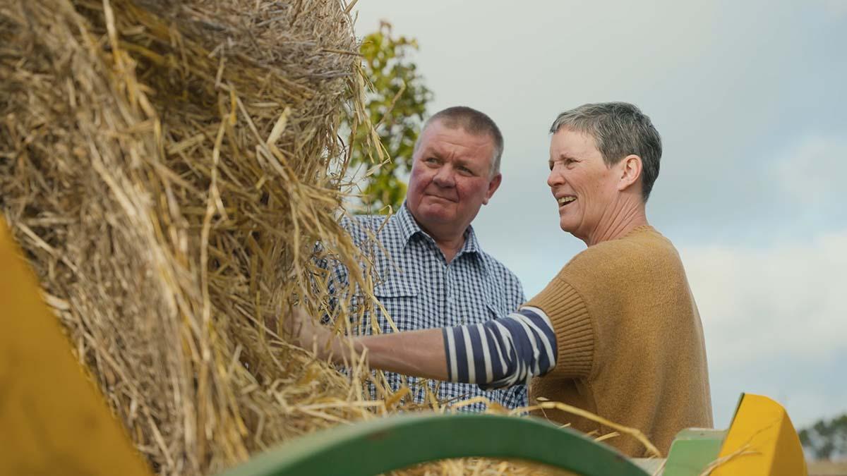 Mark and Julie Peucker standing together and smiling as they inspect a hay bale on their property